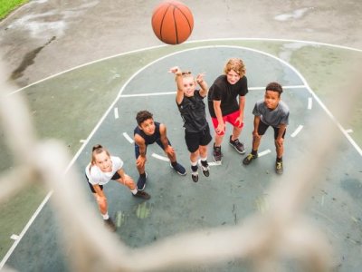 A group of teenagers standing on a basketball court in anticipation as a basketball sinks into a hoop